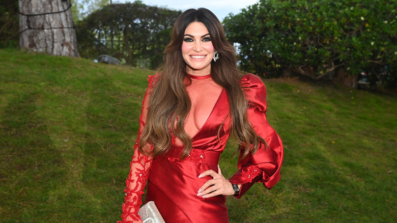 Kimberly Guilfoyle posing for photo in a red dress with greenery in background