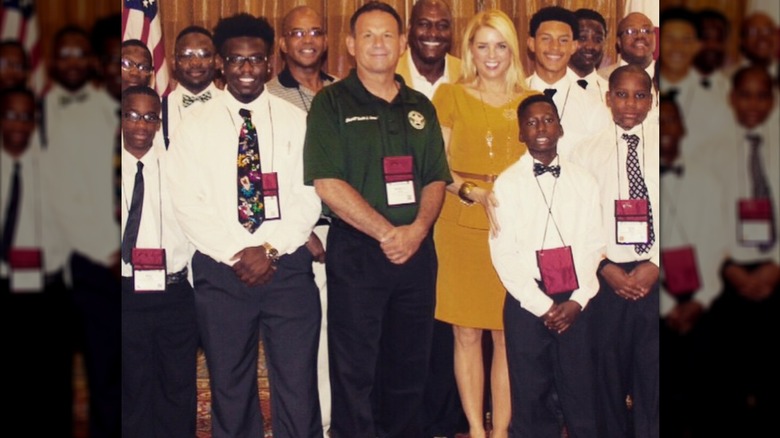 Pam Bondi wears a mustard-yellow peplum top and matching skirt while posing with a group of children and adults.