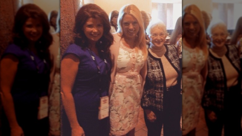 Pam Bondi wears a white and pink floral-print dress and pink cardigan while posing with Virginia Foxx and Rebecca Kleefisch.