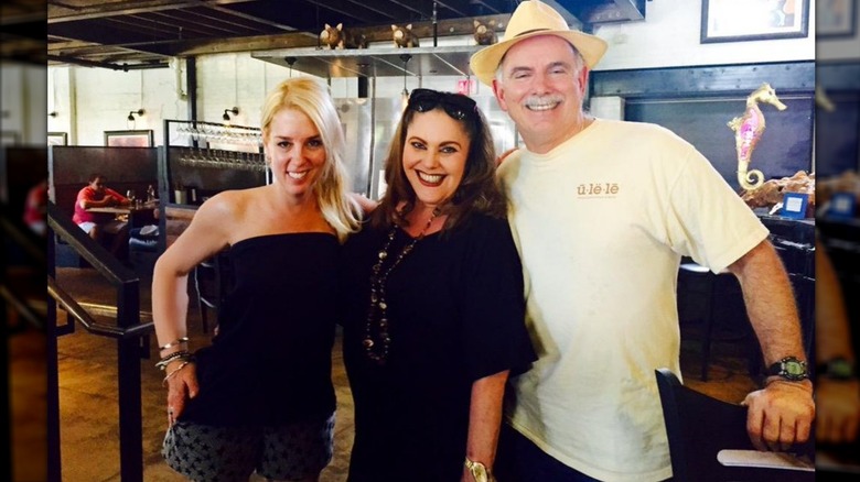 Pam Bondi wears a black tube top and gray star-print shorts while posing with two people inside a restaurant.