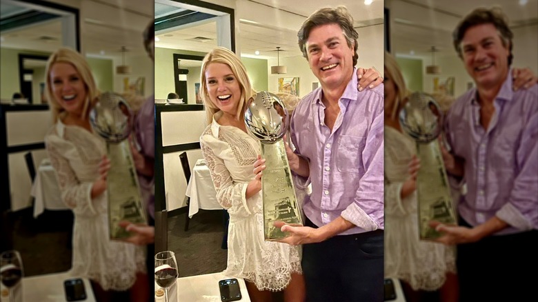 Pam Bondi wears a white collared minidress with lace details and poses with the Lombardi trophy.