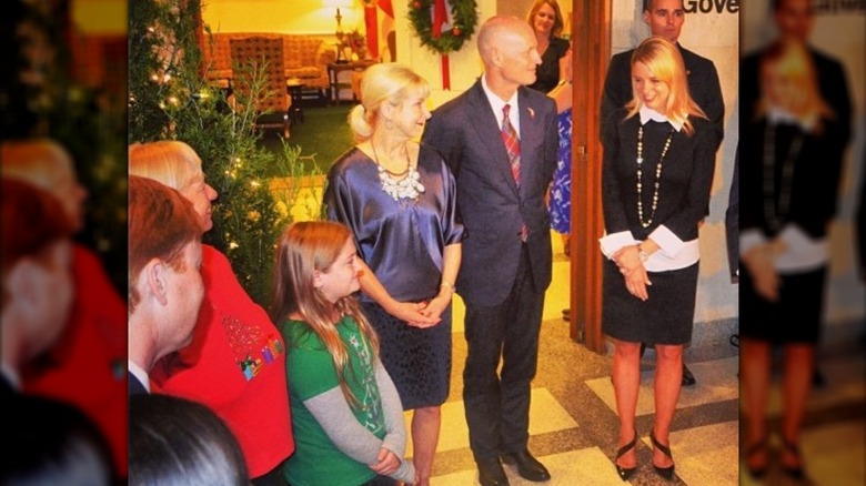 Pam Bondi wears a black skirt and black sweater over a white collared shirt at a tree dedication ceremony.