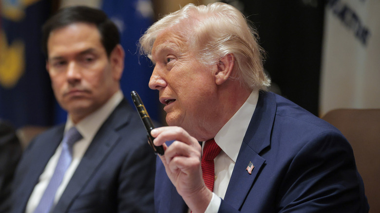 Donald Trump holds up a black Sharpie with his signature on it in gold as Marco Rubio watches him talk.