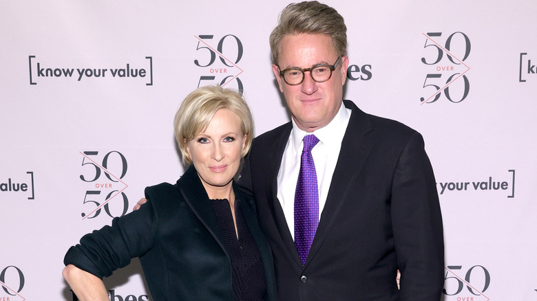 Joe Scarborough places his arm around Mika Brzezinski, as she poses with her hand on her hip.