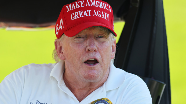 Donald Trump in MAGA hat speaking from golf cart