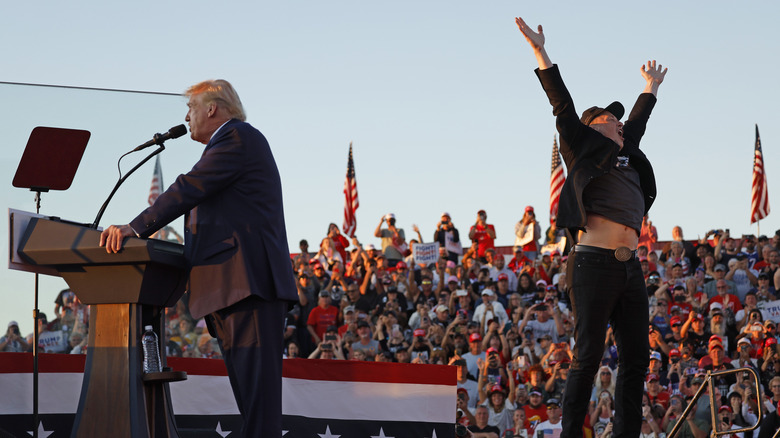Elon Musk jumping while Donald Trump gives a speech