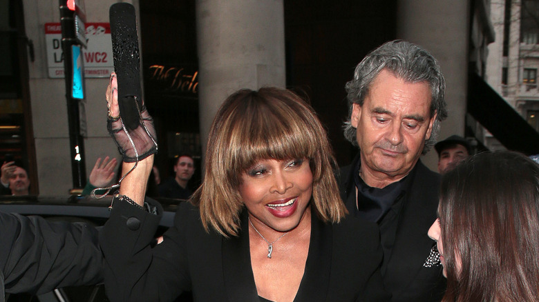 Tina Turner smiling at crowd in front as she walks in front of husband Erwin Bach