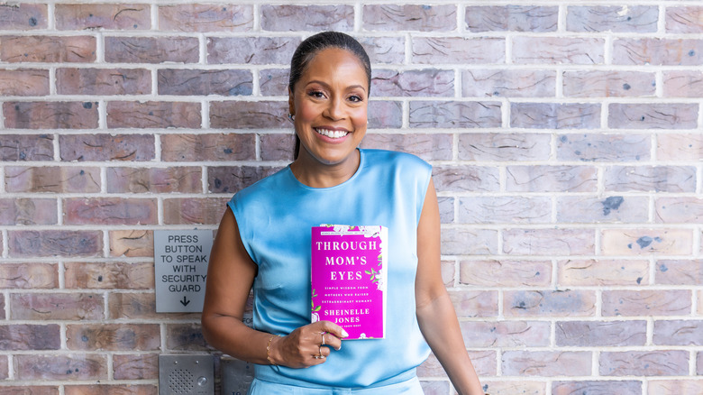 Sheinelle Jones smiling and holding her book entitled Through Mom's Eyes