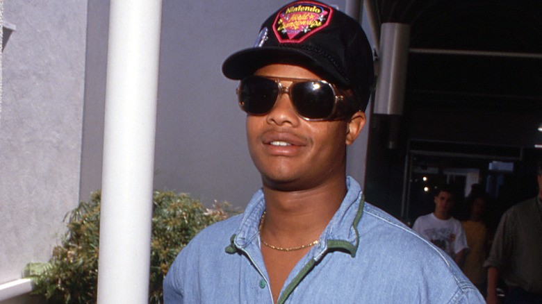 Todd Bridges smiling in a 1991 photo with a cap and sunglassees.