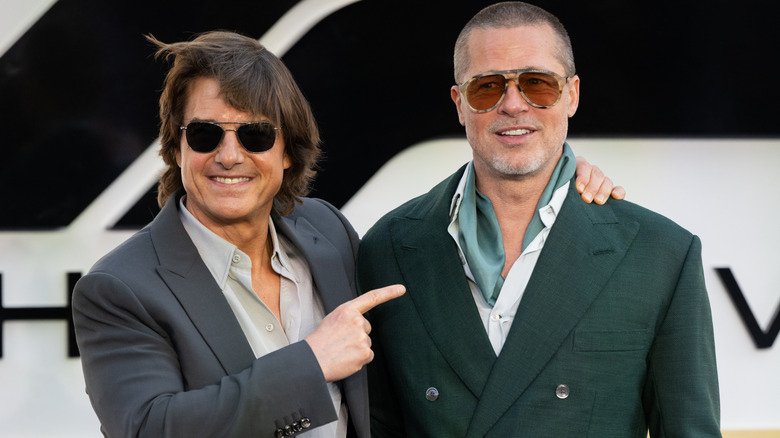 Tom Cruise pointing at Brad Pitt while both wear sunglasses and suits