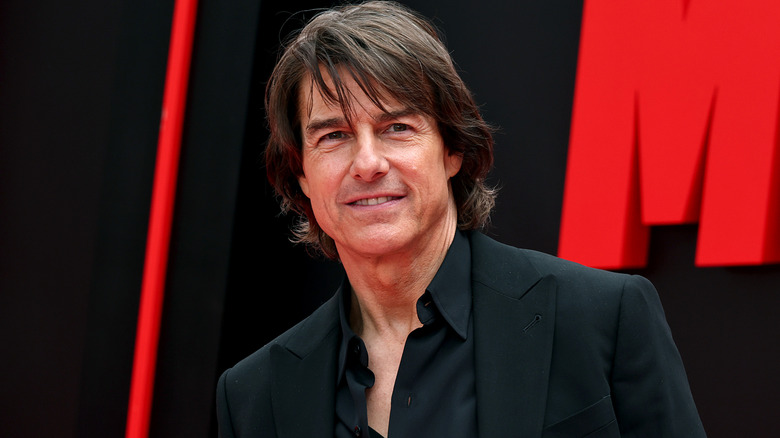 Tom Cruise smiling in front of black and red backdrop