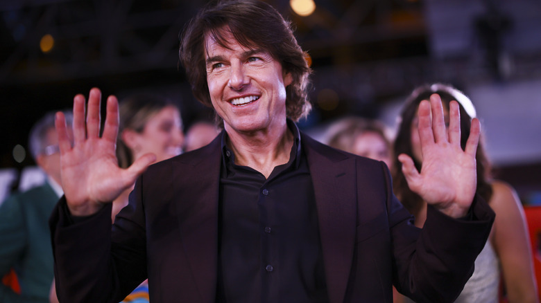 Tom Cruise smiling and holding his hands up