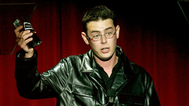 Colin Hanks accepting an award in a leather jacket and glasses