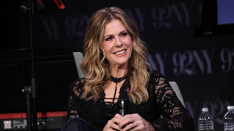 Rita Wilson smiling on stage and holding a microphone