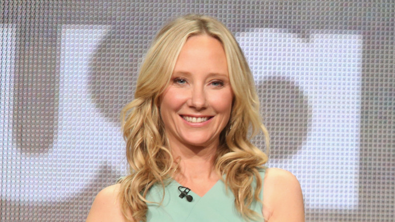 Anne Heche smiling in blonde wavy hair and light green outfit