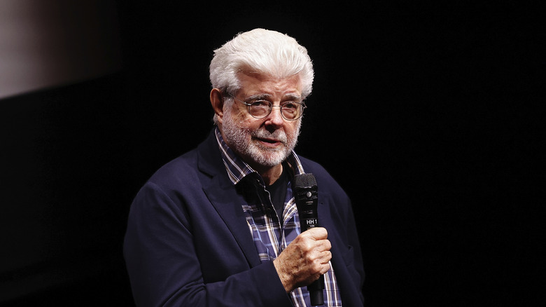 George Lucas speaking on mic in a blue checked shirt and jacket
