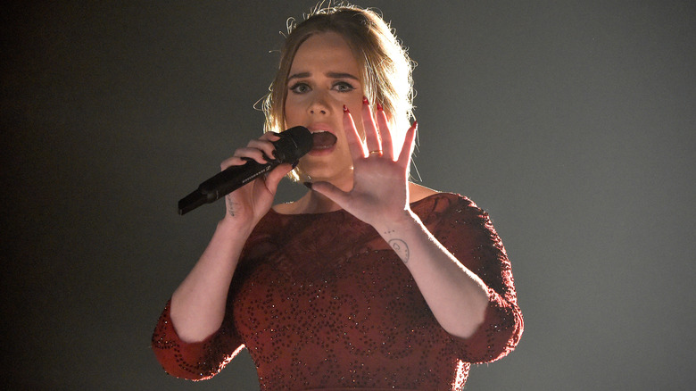 Adele singing into mic holding hand up in front of her face