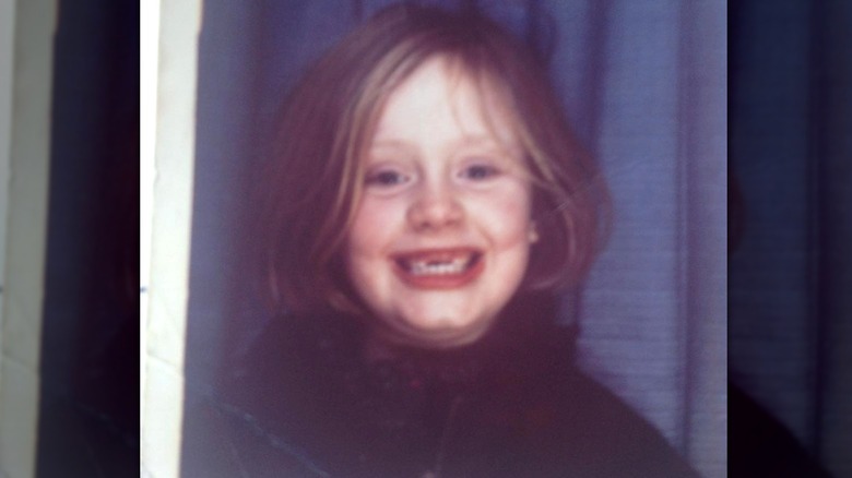 Adele as a kid smiling in a photo booth with front teeth missing