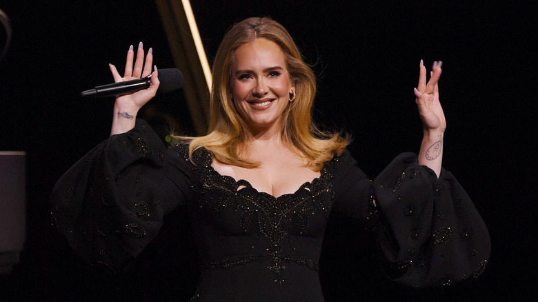 Adele smiling and waving while holding mic on stage