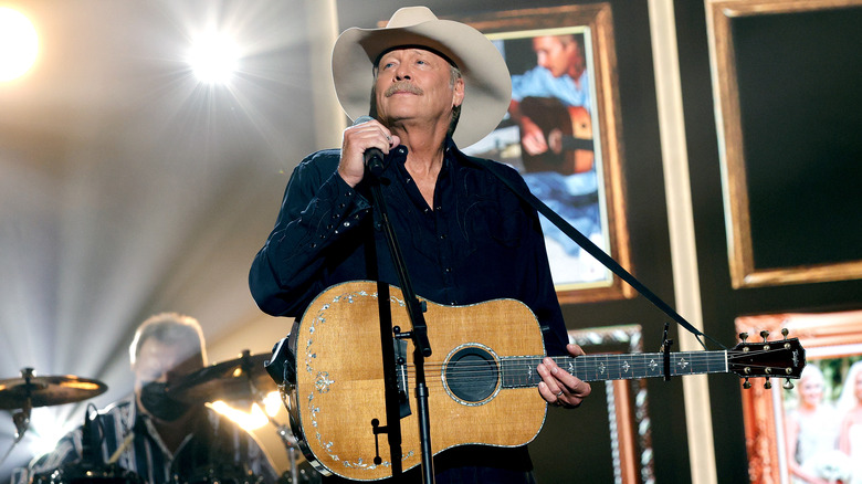 Alan Jackson in black shirt and cowboy hat holding guitar