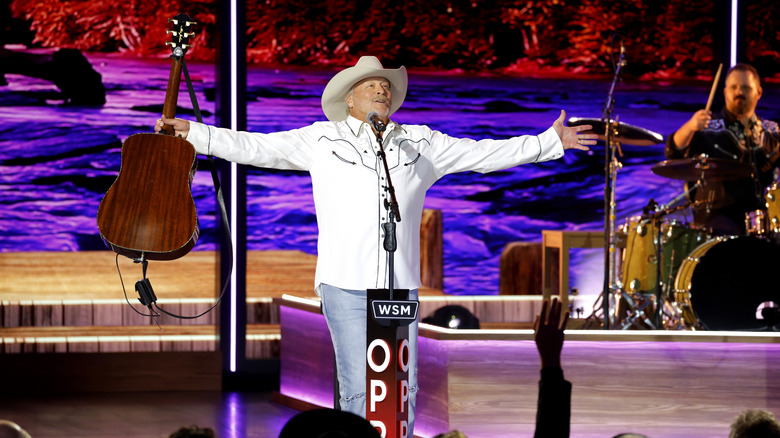 Alan Jackson in white cowboy shirt, jeans, and cowboy hat, holding his guitar