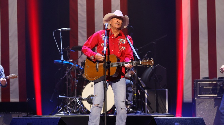 Alan Jackson perfoming in red shirt and jeans in front of American flags