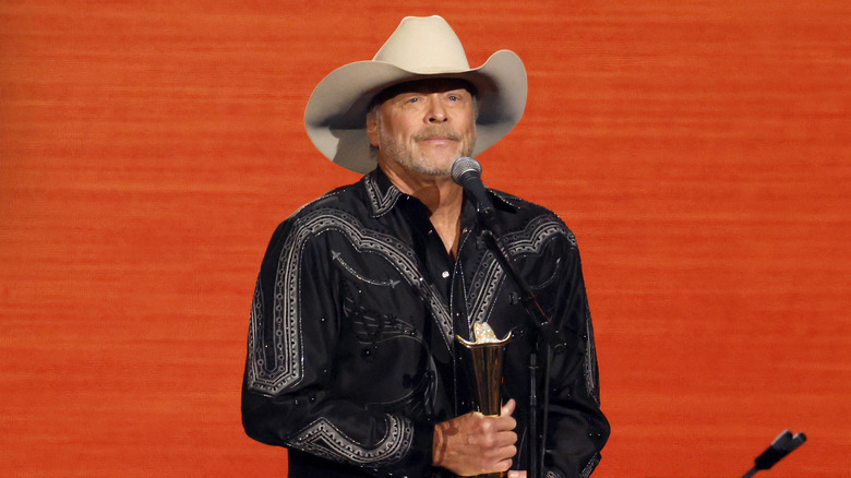 Alan Jackson in black western shirt and tan cowboy hat standing in front of mic holding an award