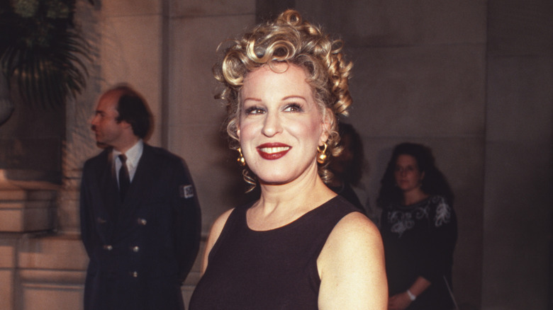 Young Bette Midler with her hair pinned up in a simple dress outside.