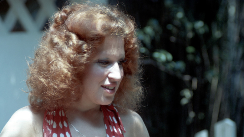 Bette Midler with red curly hair in a red and white polka dot top, outside.