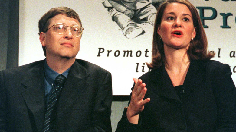 Melinda French Gates speaking at an event and sitting next to Bill Gates