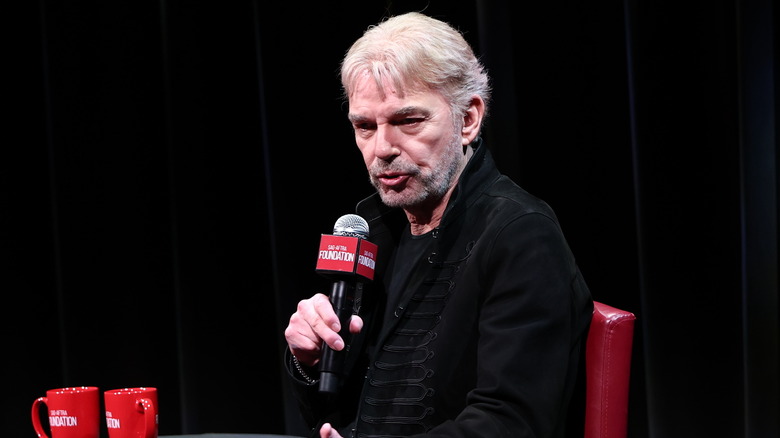 Billy Bob Thornton speaking into a microphone onstage in an all-black outfit