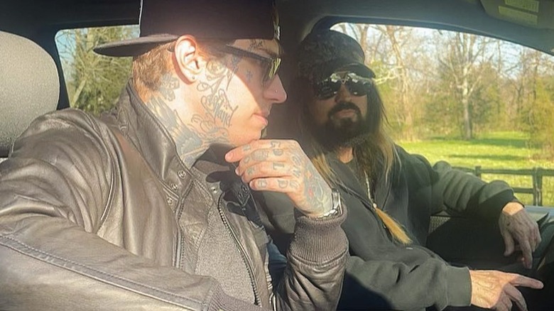 Billy Ray Cyrus in camo cap and sunglasses and black shirt with Trace Cyrus in black leather jacket and sunglasses walking outside