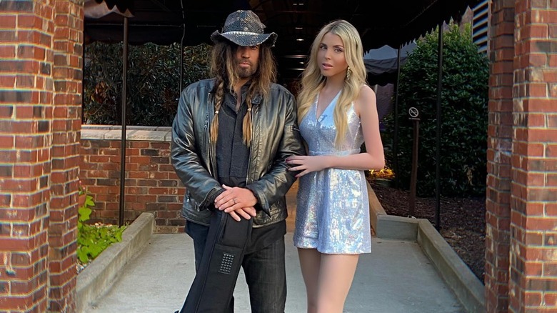 Billy Ray Cyrus in black hat and Firerose in short silver dress in front of Grand Ole Opry entrance