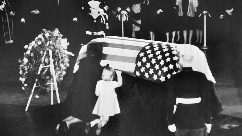 Jacqueline Kennedy and daughter Caroline kneeling next to the flag-draped casket of John F. Kennedy
