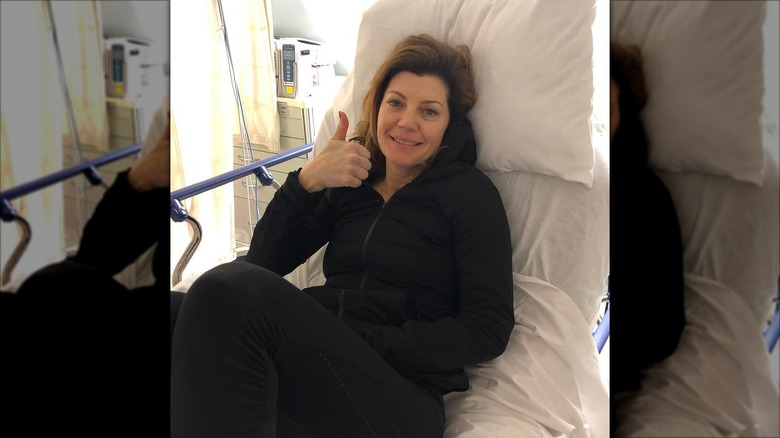 Norah O'Donnell giving a thumbs up makeup free in a hospital bed.