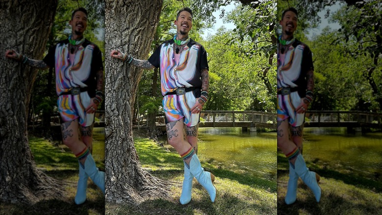 David Bromstad leaning against tree rainbow outfit