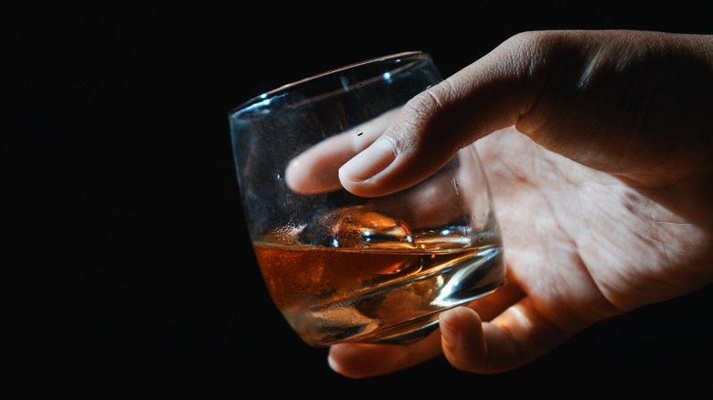 A hand holding a glass of whiskey