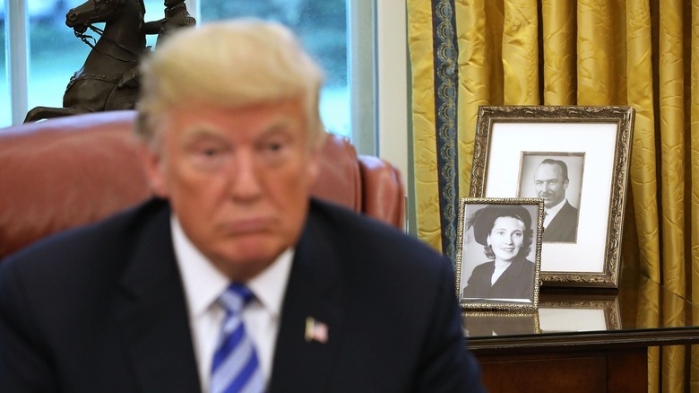 Donal Trump in the Oval Office, with photographs of his parents behind