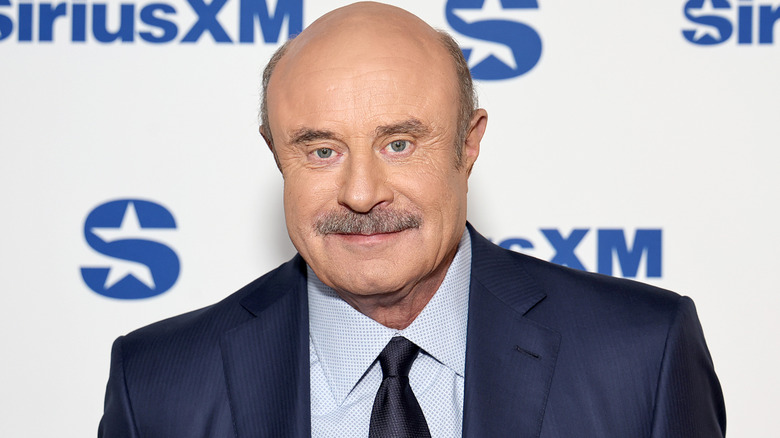 Phil McGraw in front of white backdrop with blue text