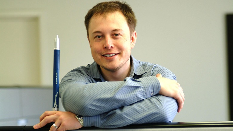 A young Elon Musk holding a model of a SpaceX rocket