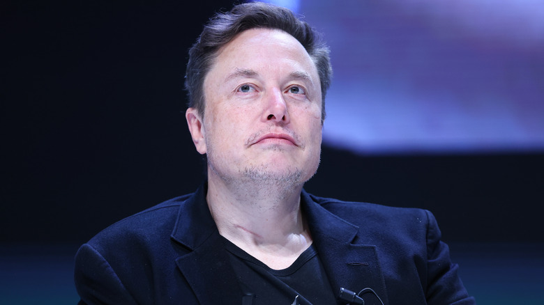 Elon Musk looking wistful in a black suit jacket and black T-shirt