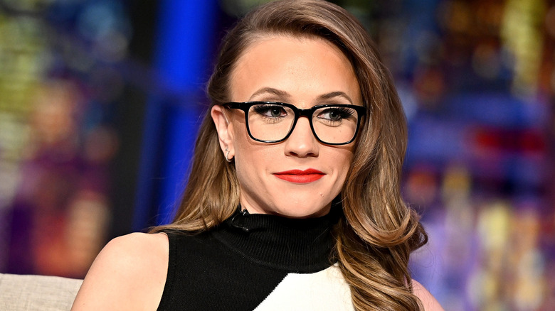 Kat Timpf smiling while wearing glasses, red lipstick, and a sleeveless monochrome top