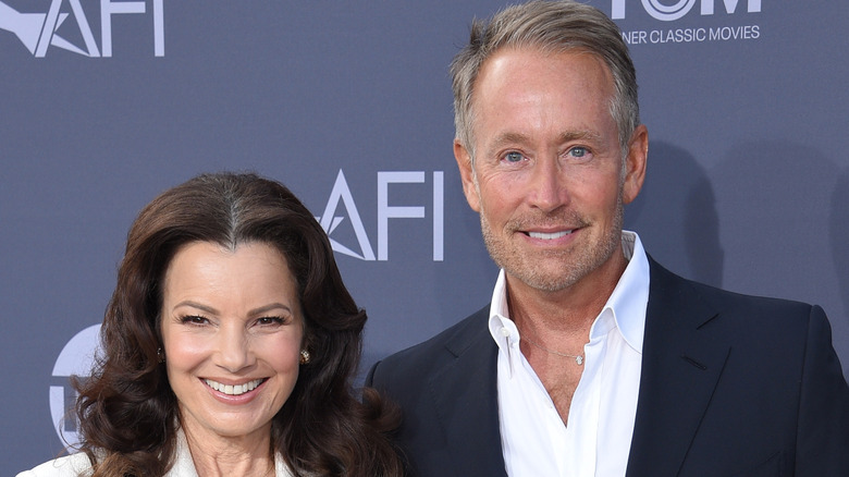 Fran Drescher wearing a white suit posing next to Peter Marc Jacobson who's wearing a black blazer and white collared shirt at the AFI Lifetime Achievement Awards.