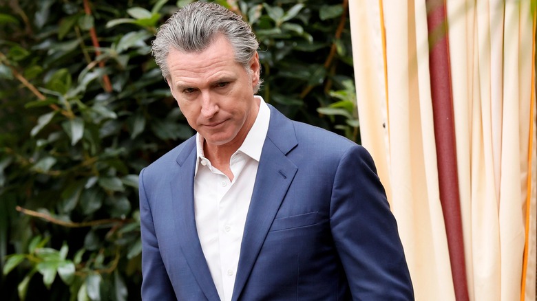 Gavin Newsom grimacing in a navy suit with a white shirt underneath