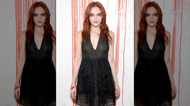 Madeline Brewer with long red hair in black sleeveless low cut dress