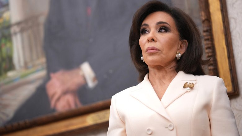 Jeanine Pirro looking serious in a white blazer with pearl earrings and a gold eagle brooch