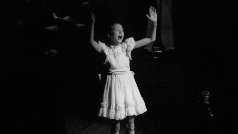 Young Julie Andrews singing dramatically with arms raised