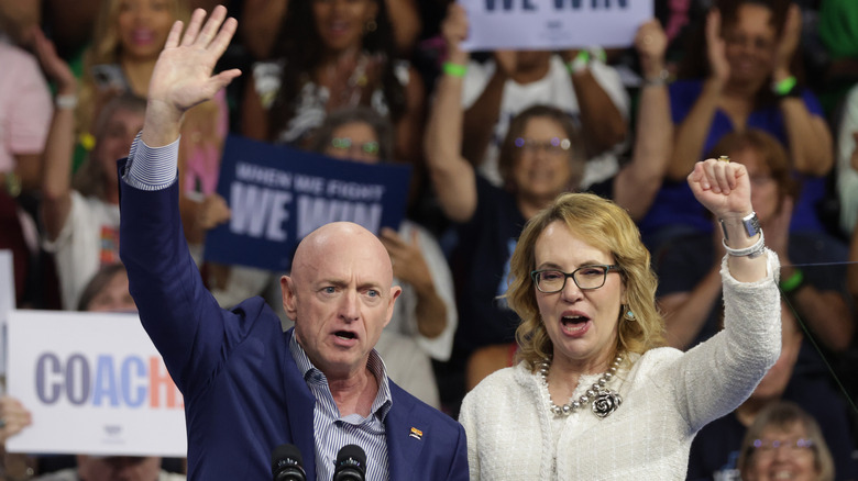 Gabby Giffords and Mark Kelly cheering while holding their arms up at a rally