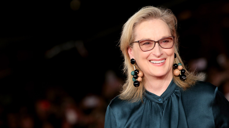 Meryl Streep smiling in brown glasses and dramatic dangling earrings