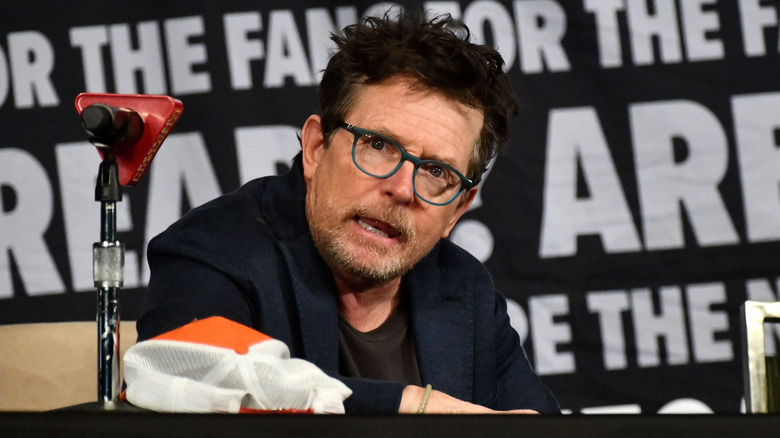 Michael J. Fox onstage at an event in glasses and a black blazer